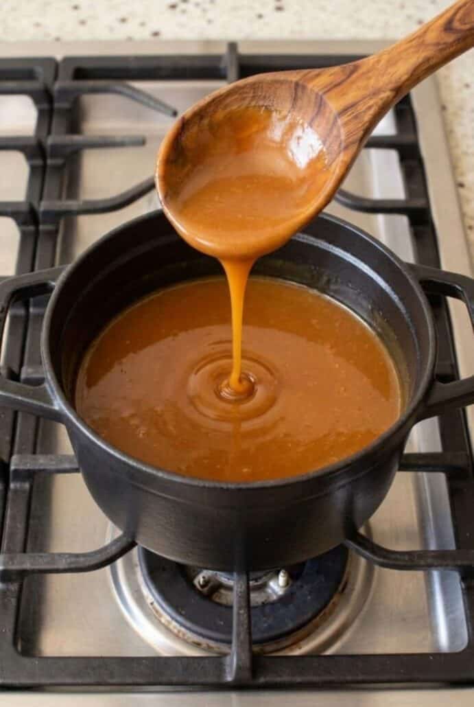 Smooth homemade caramel sauce dripping from a spoon into the saucepan.
