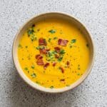 Overhead view of creamy carrot soup garnished with crispy bacon and parsley.