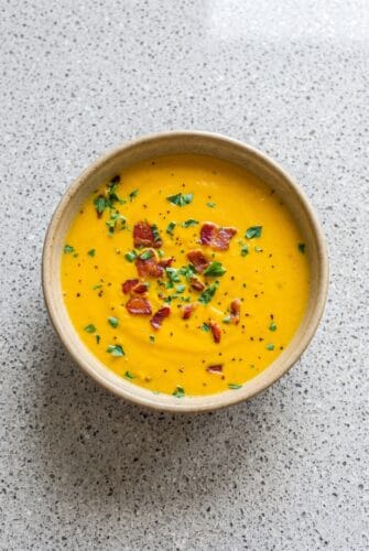 Creamy Carrot Soup Recipe With Bacon Overhead view of creamy carrot soup garnished with crispy bacon and parsley.