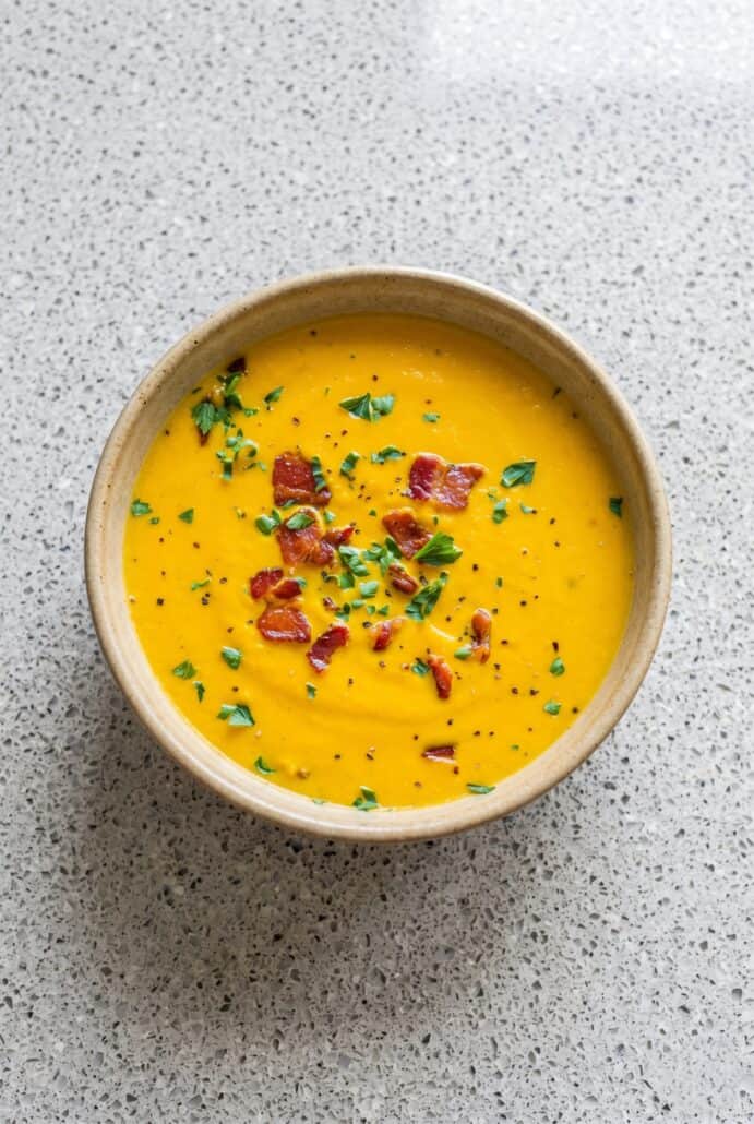 Overhead view of creamy carrot soup garnished with crispy bacon and parsley.