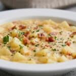 Close-up of creamy clam chowder with tender potatoes, bacon bits, and fresh chives.