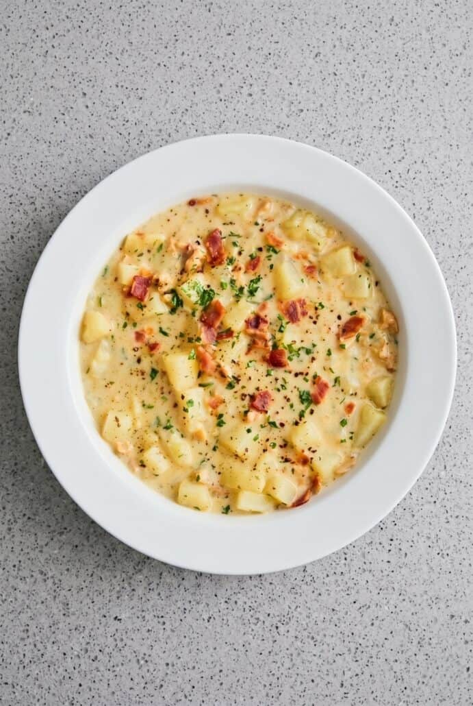 Bowl of creamy clam chowder garnished with crispy bacon and fresh chives.