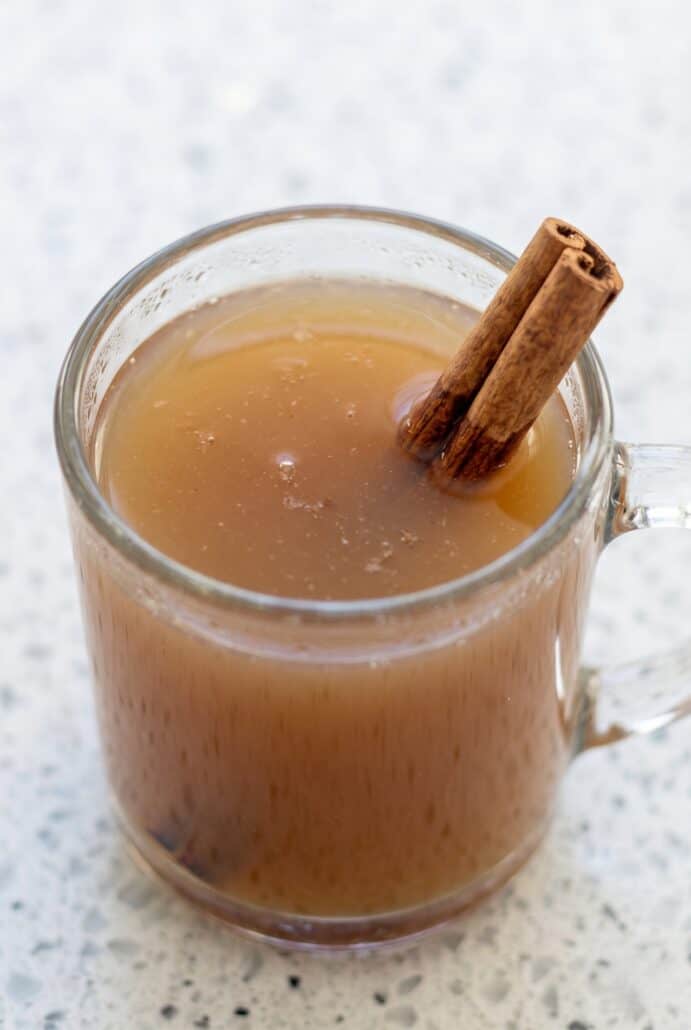 Homemade apple cider in a glass mug with a cinnamon stick on top.