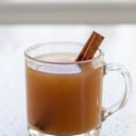 Hot homemade apple cider in a glass mug with cinnamon stick garnish.