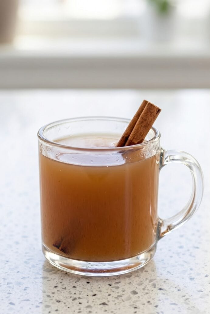 Hot homemade apple cider in a glass mug with cinnamon stick garnish.