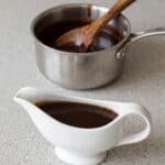 Homemade chocolate syrup in a serving pitcher with saucepan in the background.