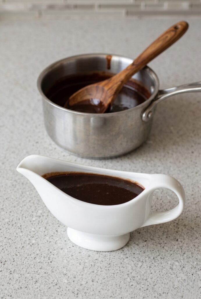 Homemade chocolate syrup in a serving pitcher with saucepan in the background.