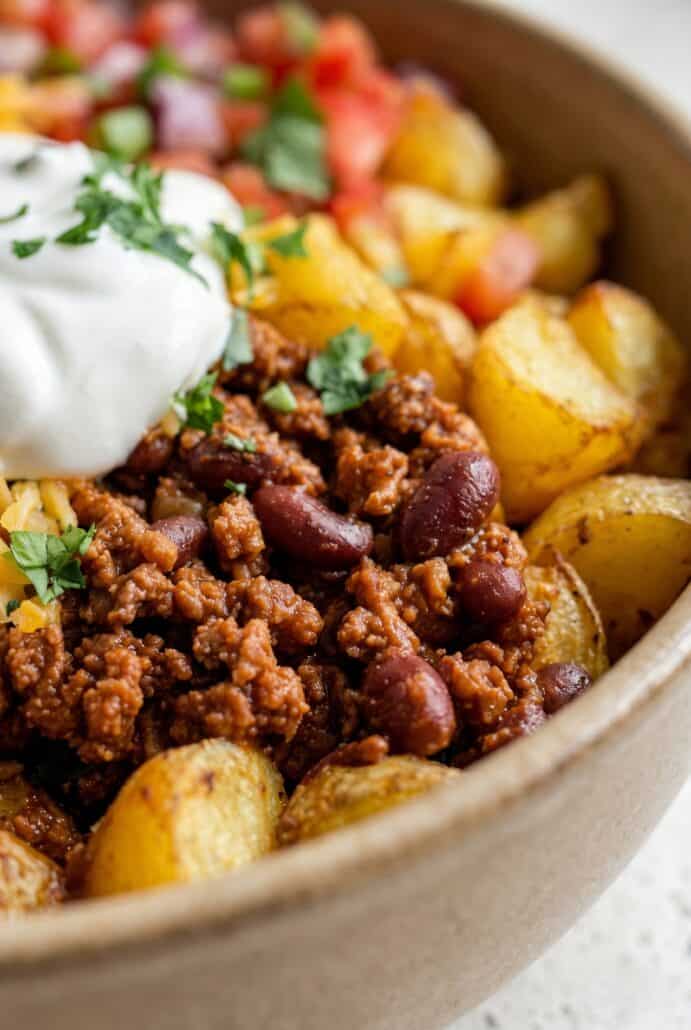 Close-up of Loaded Potato Taco Bowl with seasoned taco meat, black beans, crispy roasted potatoes, and sour cream.