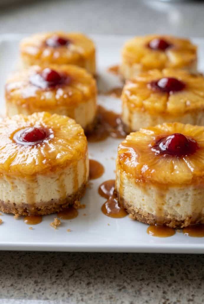 Mini pineapple upside-down cheesecakes with pineapple, cherry, and caramel topping.