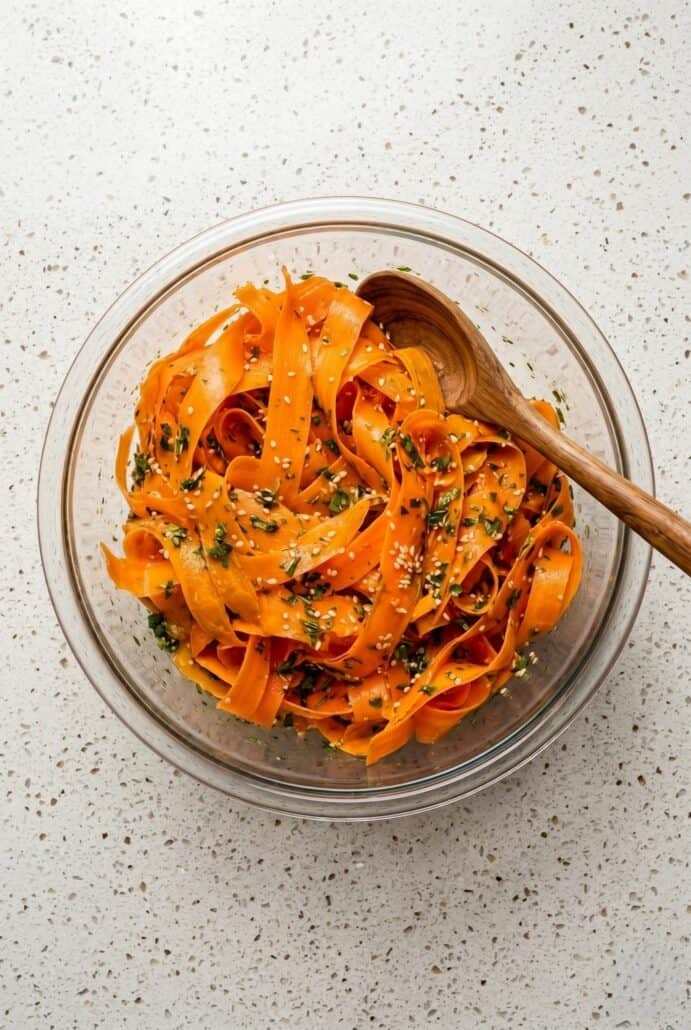 Raw carrot salad in a glass bowl with carrot ribbons, herbs, and sesame seeds.