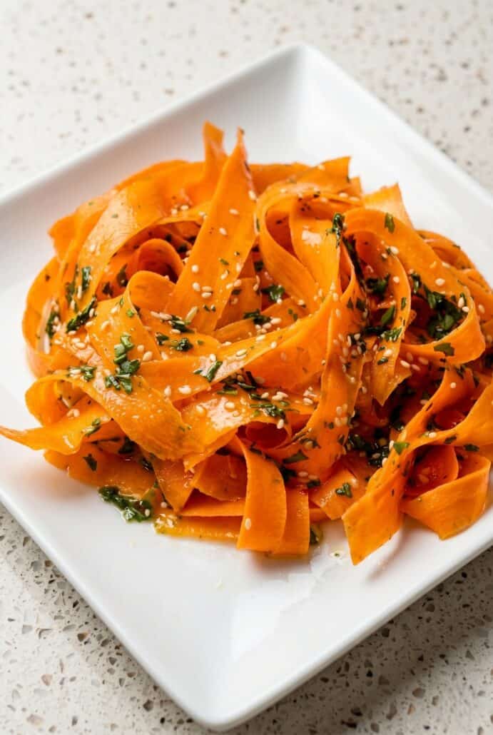 Close-up of raw carrot salad with fresh carrot ribbons, herbs, and sesame seeds.
