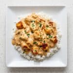 Smothered chicken and rice with creamy sauce and parsley on a white plate.