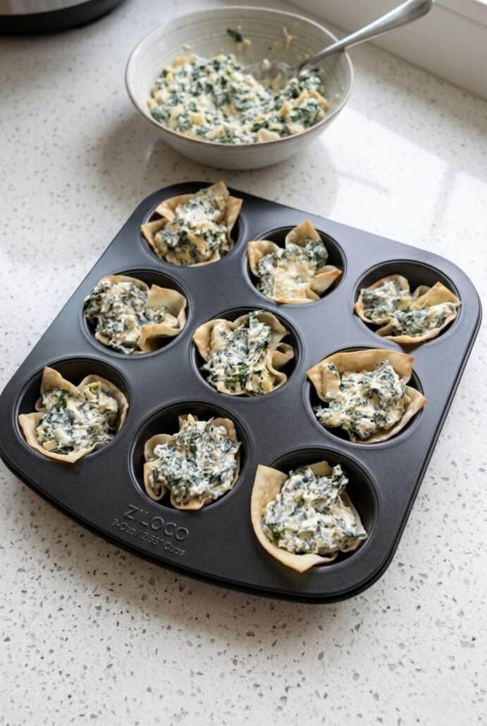Spinach artichoke wonton cups baking in a muffin tin until golden and crispy.