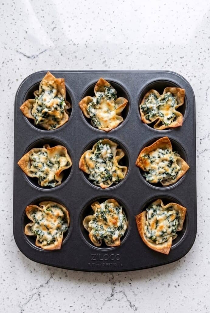 Baked spinach artichoke wonton cups in a muffin tin with crispy golden wrappers.