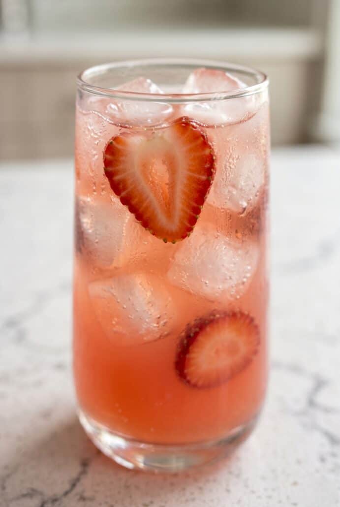Close-up of a glass of strawberry soda with ice and fresh strawberry slices, highlighting a refreshing homemade summer drink recipe.