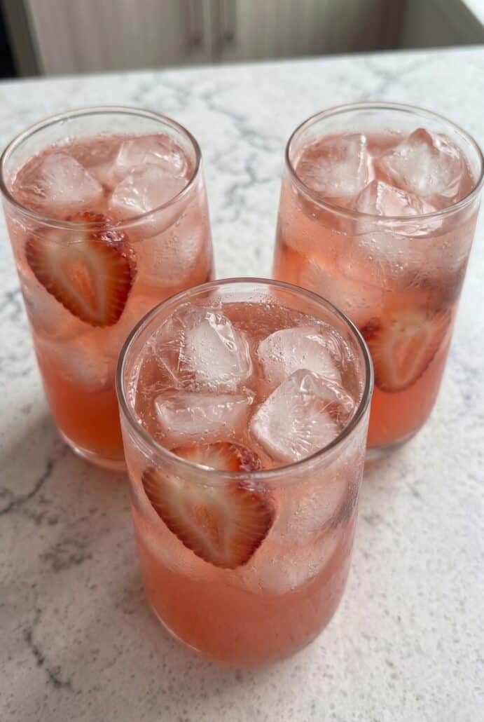 Glasses of homemade strawberry soda with ice and fresh strawberry slices, perfect for a refreshing summer drink recipe.