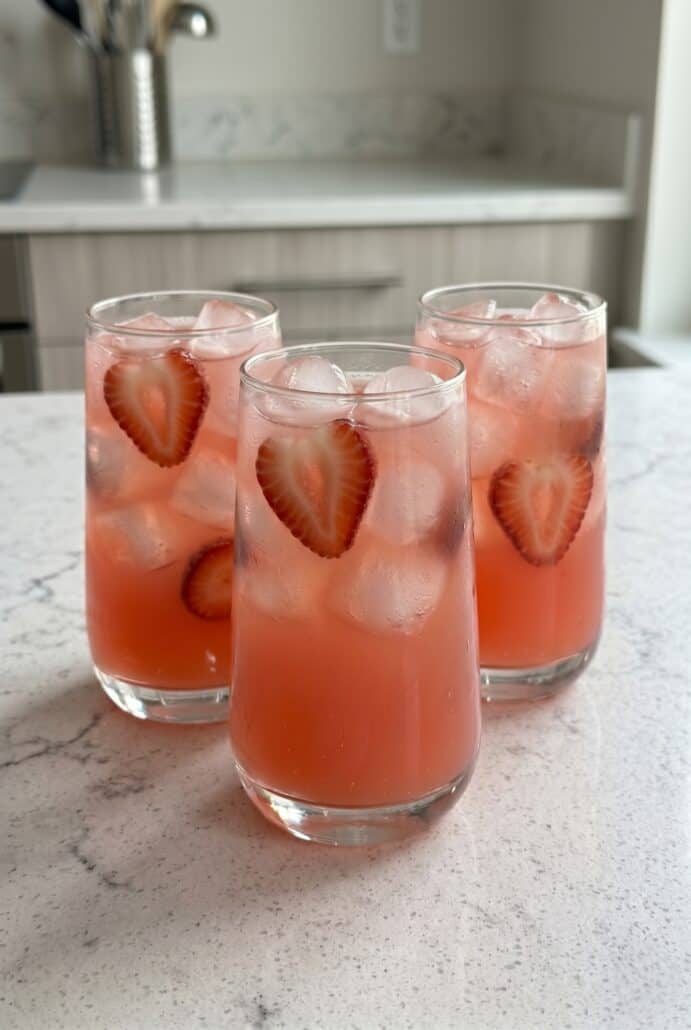 Strawberry soda in ice-filled glasses with fresh strawberry slices, perfect for a refreshing homemade summer drink recipe.