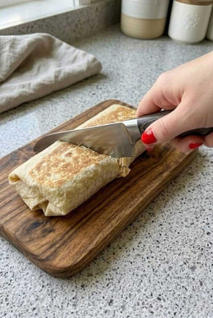 Sliced crispy tuna melt wrap on a cutting board with creamy tuna and melted cheese filling.