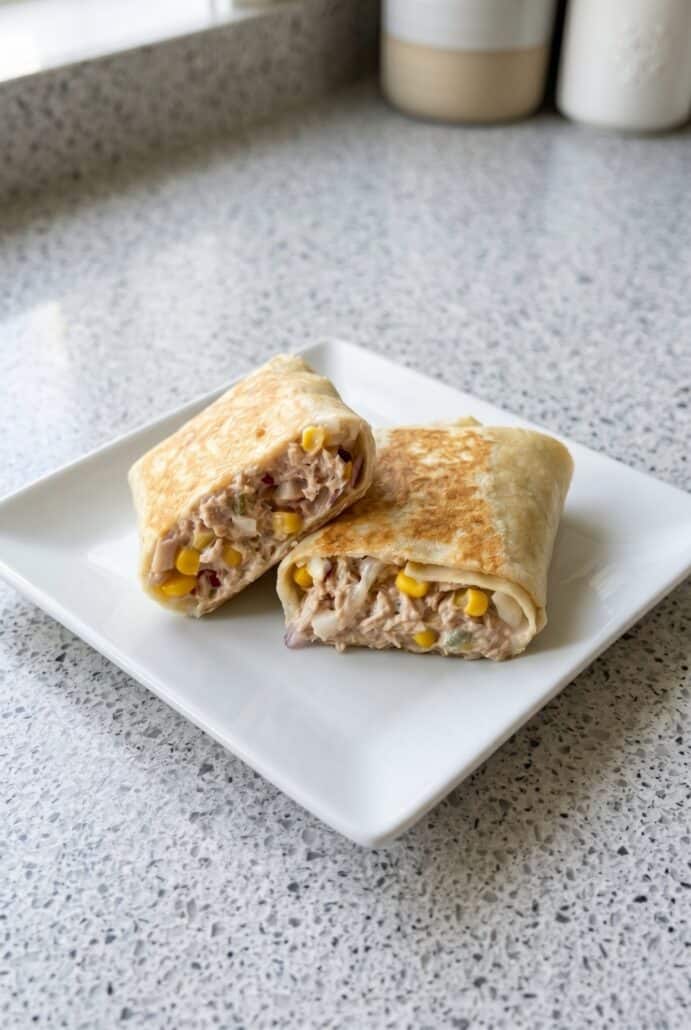 Tuna melt wrap halves on a plate with creamy tuna, corn, and melted cheese filling.