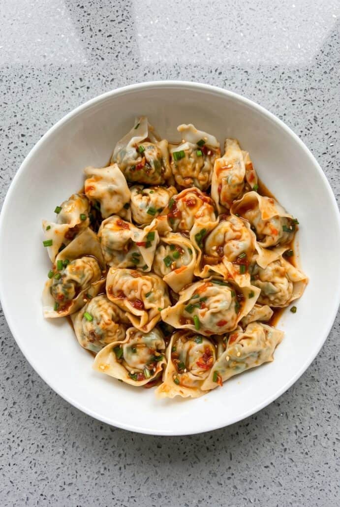 Top view of vegan tofu and chive wontons drizzled with chili oil, served in a bowl.