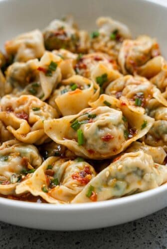 Tofu and Chive Wontons in Spicy Chili Broth Bowl of vegan tofu and chive wontons in spicy chili broth topped with scallions and chili oil.