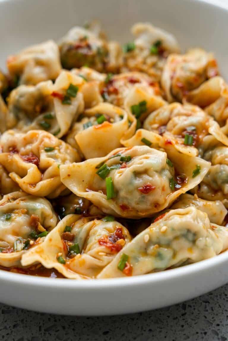 Bowl of vegan tofu and chive wontons in spicy chili broth topped with scallions and chili oil.