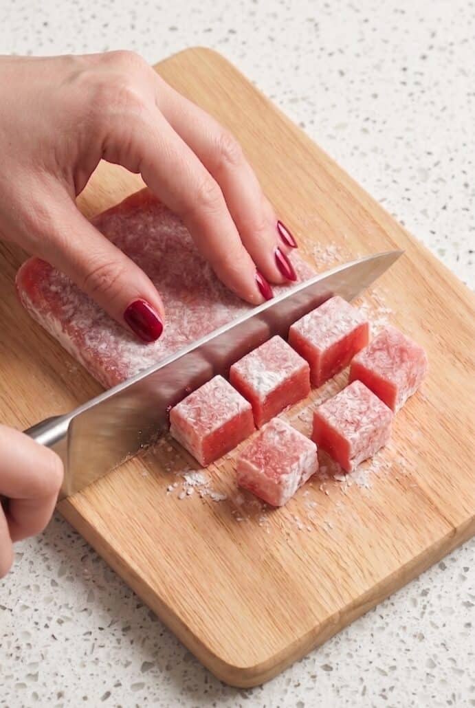 Knife cutting chilled watermelon mochi into bite-sized pieces.