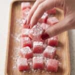 Hands showing sliced watermelon mochi dusted with flour for serving.