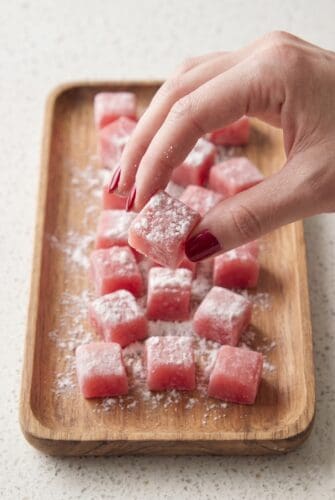 Hands showing sliced watermelon mochi dusted with flour for serving.