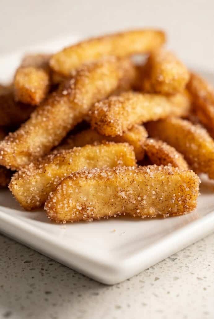 Crispy air fryer apple fries coated in cinnamon sugar on a plate.