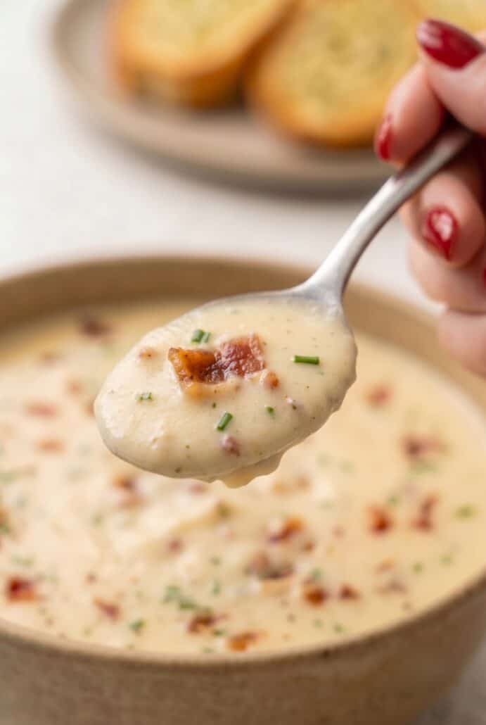 Spoonful of creamy baked potato soup with bacon and chives for a cozy homemade dinner.