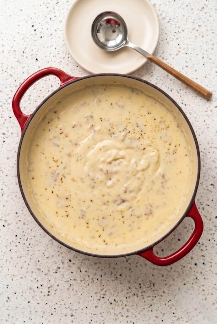 Creamy baked potato soup simmering in a red Dutch oven for an easy homemade comfort food dinner.