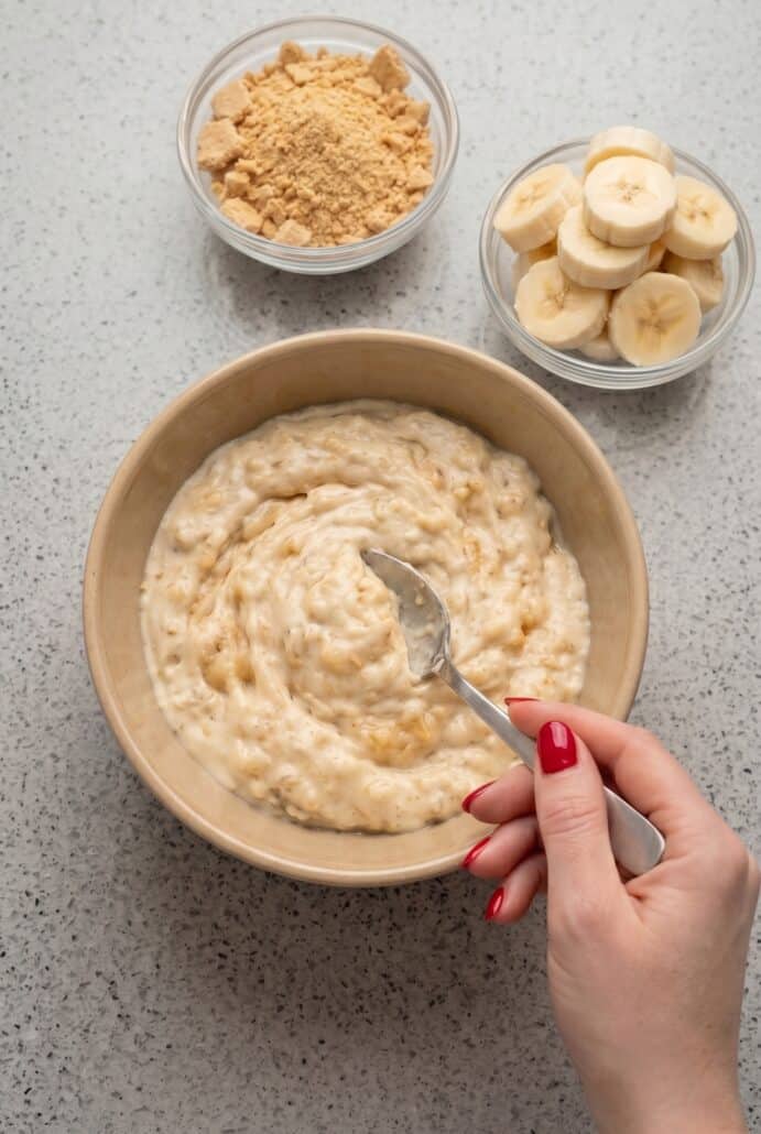 Mixing creamy Banana Pudding Yogurt in a bowl with banana slices and graham cracker crumbs ready to add.