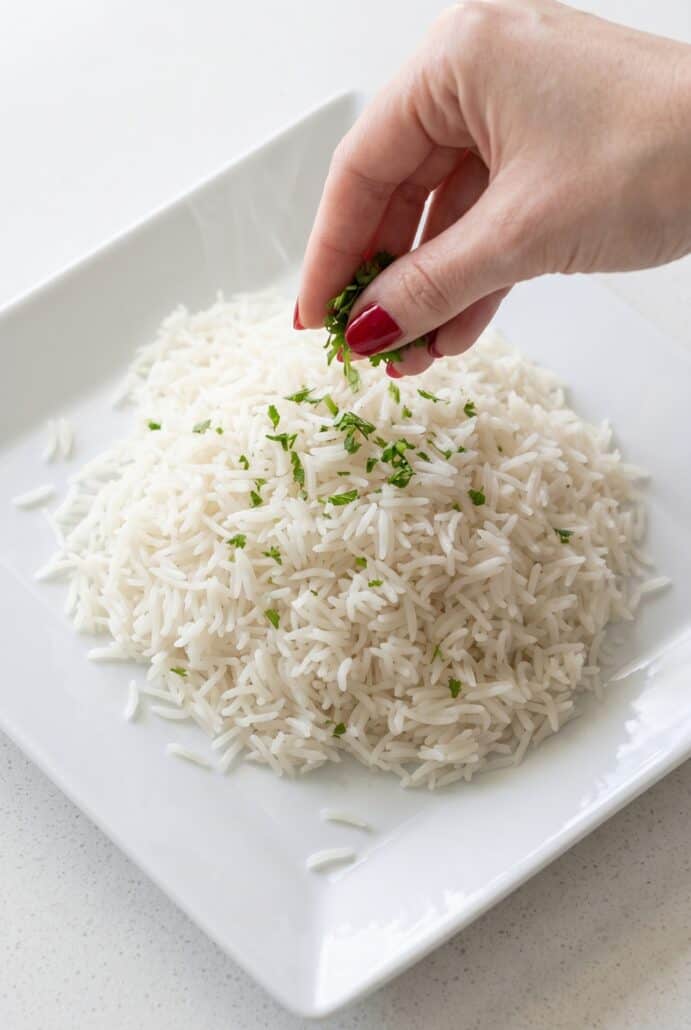 Fluffy basmati rice garnished with fresh herbs on a white plate.
