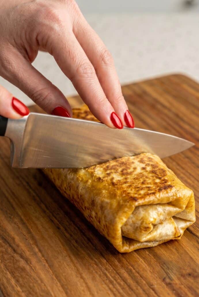 Slicing a crispy baked beef and cheese chimichanga filled with seasoned ground beef and melted cheese.