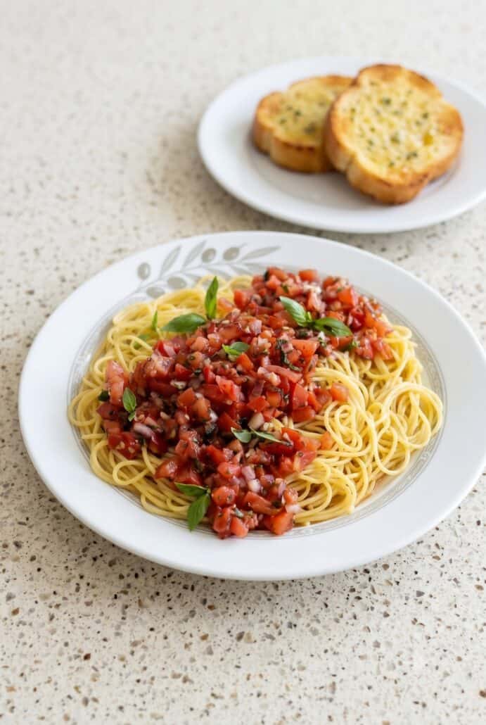 Bruschetta pasta salad with spaghetti, tomato basil topping, and garlic bread on the side.