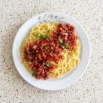Bruschetta pasta salad with spaghetti, fresh tomatoes, basil, and balsamic glaze on a white plate.