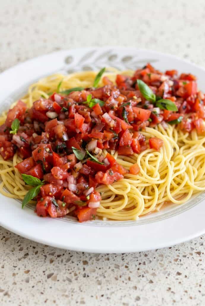 Close-up of bruschetta pasta salad with spaghetti, fresh tomato basil topping, and balsamic glaze.