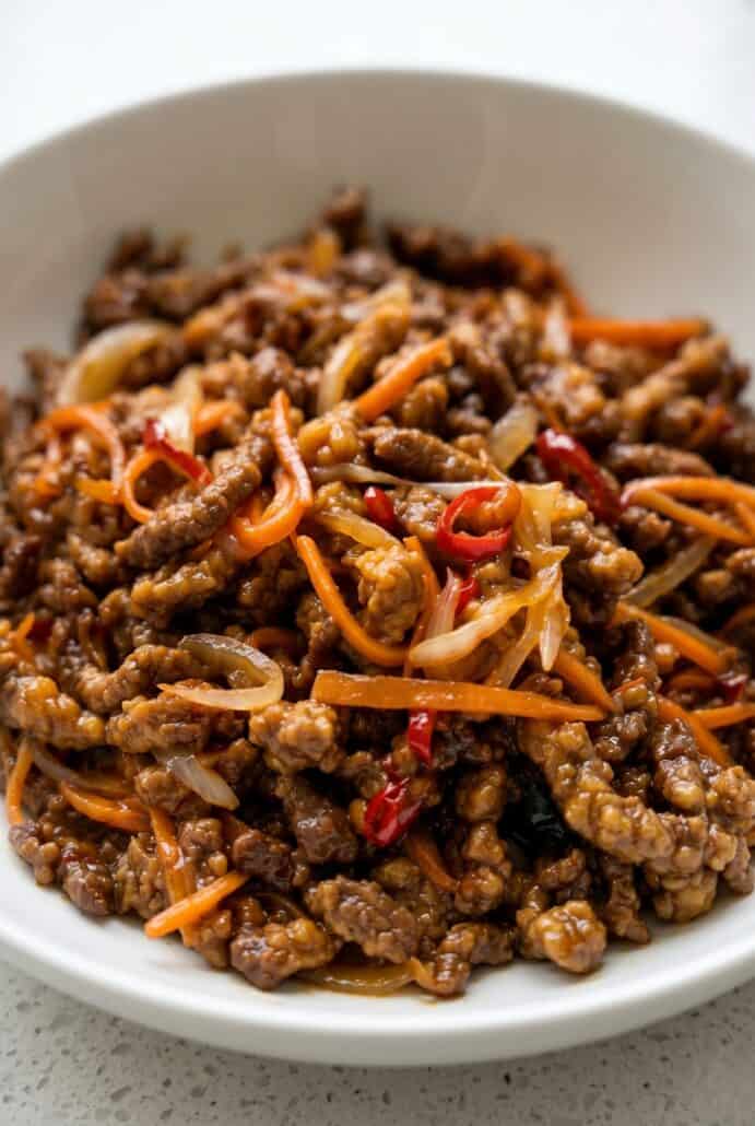 Close-up of crispy chilli beef with carrots and red chilli in sticky sauce.