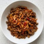 Crispy chilli beef served in a white bowl with carrots and red chilli.