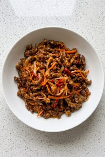 Crispy Chilli Beef – A Sweet, Spicy & Sticky Dinner Recipe Crispy chilli beef served in a white bowl with carrots and red chilli.