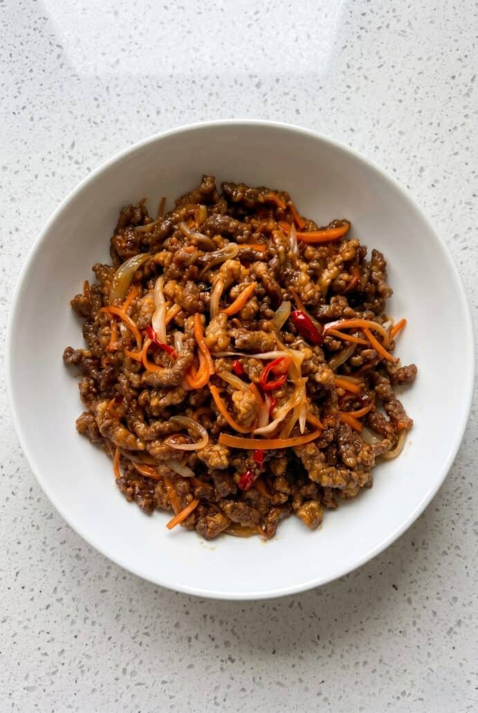 Crispy chilli beef served in a white bowl with carrots and red chilli.