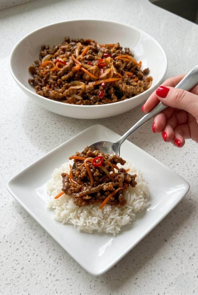 Spoonful of crispy chilli beef being served over white rice.