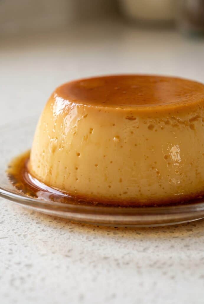 Side view of eggless caramel pudding with glossy caramel sauce on a dessert plate.