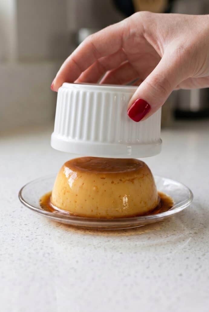 Eggless caramel pudding being unmolded from a ramekin onto a plate.