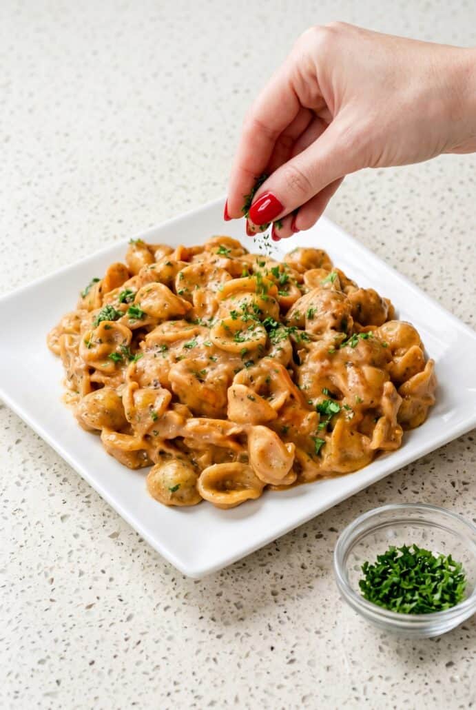 Hand sprinkling parsley over creamy French Onion Pasta with caramelized onions and cheese for serving.