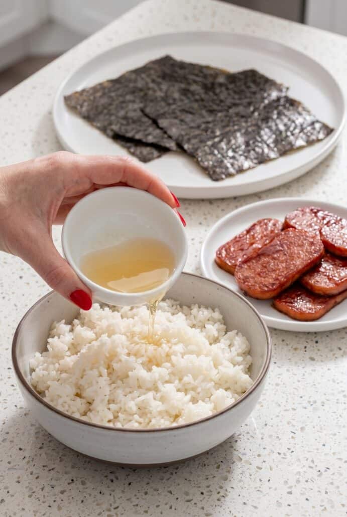 Seasoning cooked sushi rice with vinegar mixture for homemade Hawaiian Spam musubi.