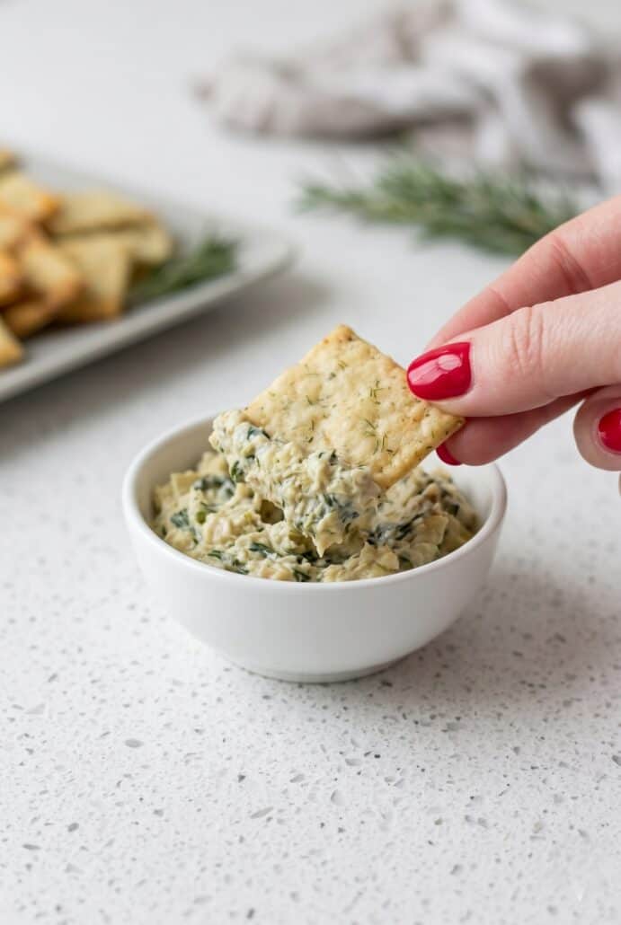 Rosemary sea salt cracker dipped into a creamy spread for an easy homemade appetizer.