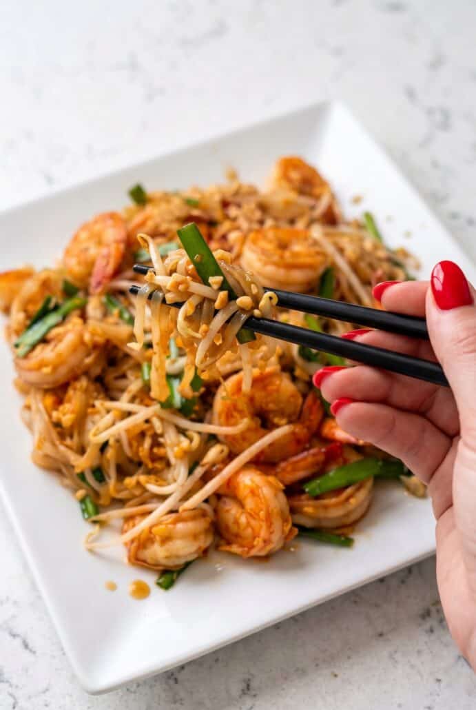 Shrimp Pad Thai with chopsticks lifting noodles, shrimp, bean sprouts, and peanuts.