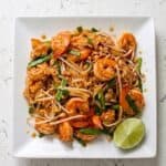 Plate of Shrimp Pad Thai with rice noodles, shrimp, bean sprouts, peanuts, and lime wedge.